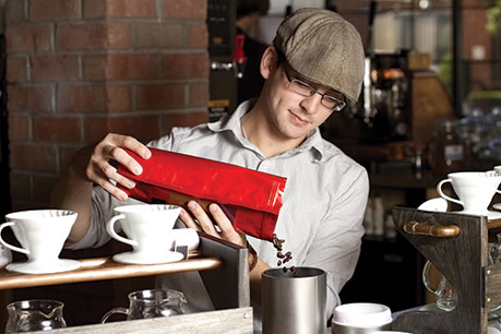 Photo shows Eddie Walker pouring coffee seeds into a carafe.