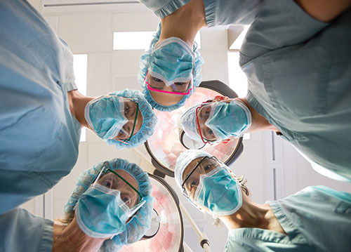 Photo shows 5 masked surgeons looking into a camera in an operation theatre.