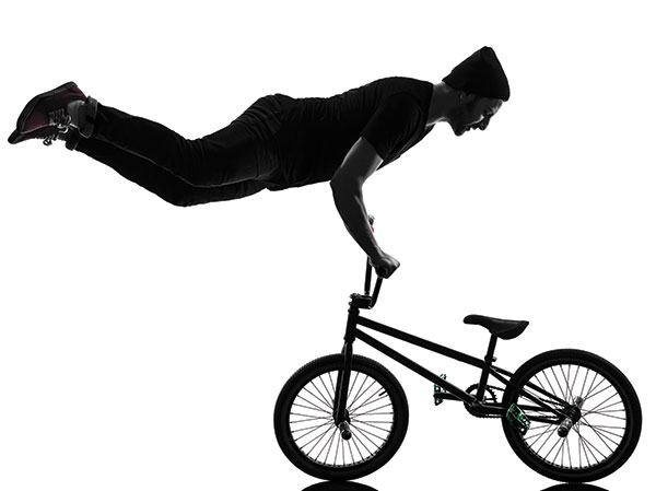 Photo shows a man doing a handstand on the handlebars of a bicycle.