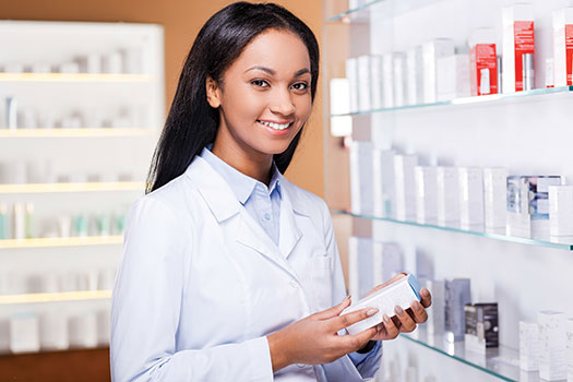 Photo shows a woman in a white outfit holding a small box, standing next to a display of similar product boxes.