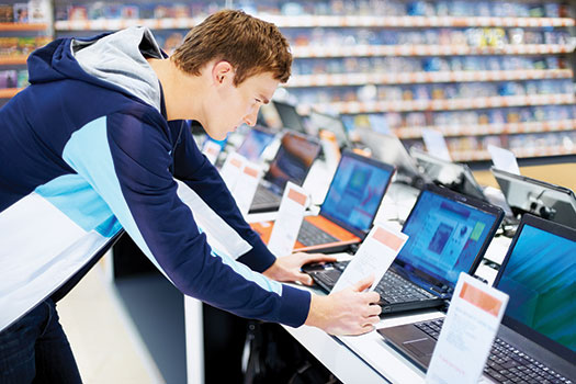 Photo shows a man standing in front of a display of laptops and reading a card in front of one of them.