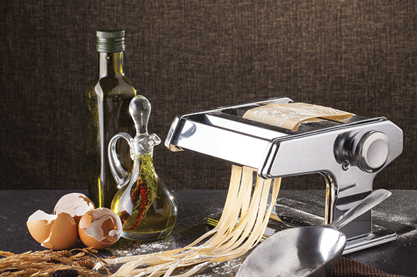 Photo shows pasta coming out of a pasta-maker, with eggs and oil next to the machine.