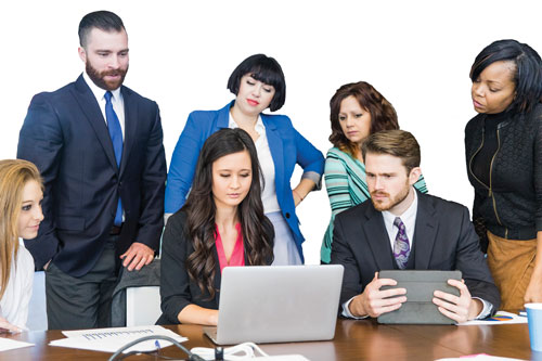 Photo shows several people in an office, looking at the laptop screen of a woman sitting in the center.