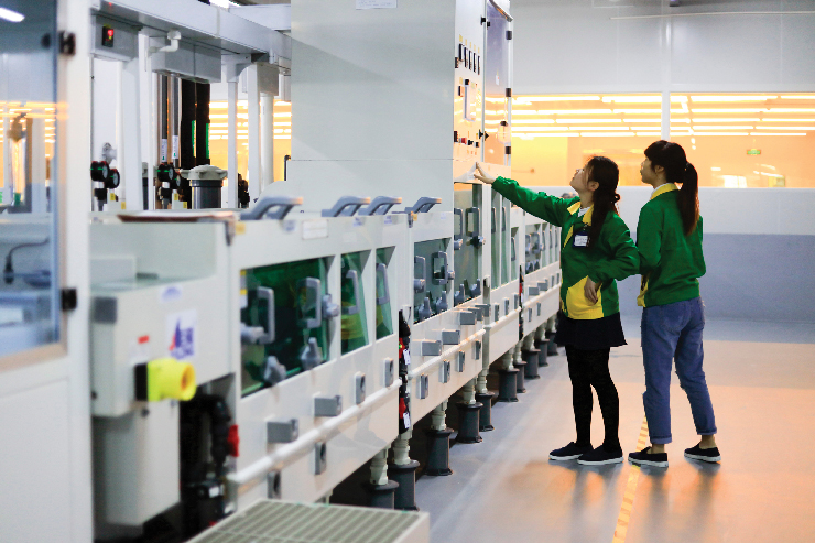 A photo of two Asian women workers inside a plant manufacturing electronic parts.