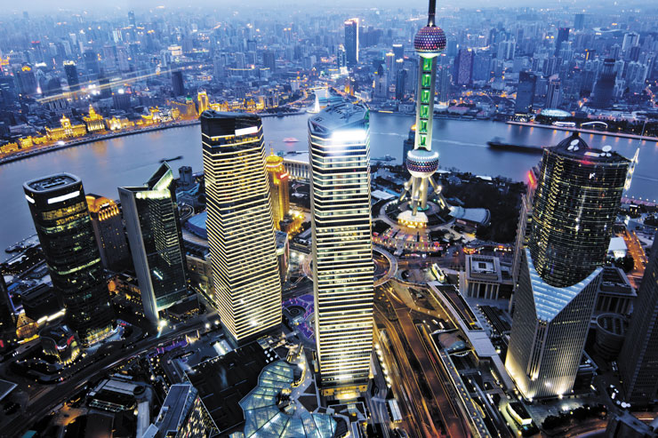 A photo of Shanghai by night, with the river flowing in the middle and with many skyscrapers spread around.