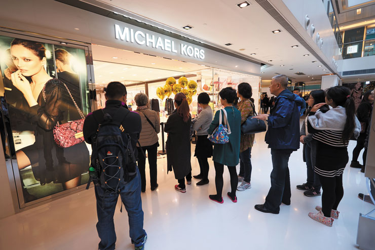 Photo of several shoppers waiting in a line to enter a Michael Kors store.