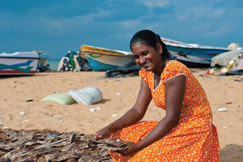 Photo showing a woman seated on beach sand.