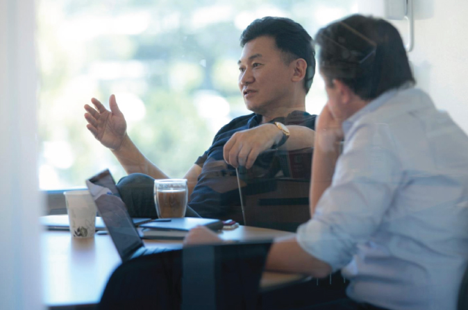 Photo illustration of two men (both seated; one of the man's back is only seen) in a discussion over a coffee.