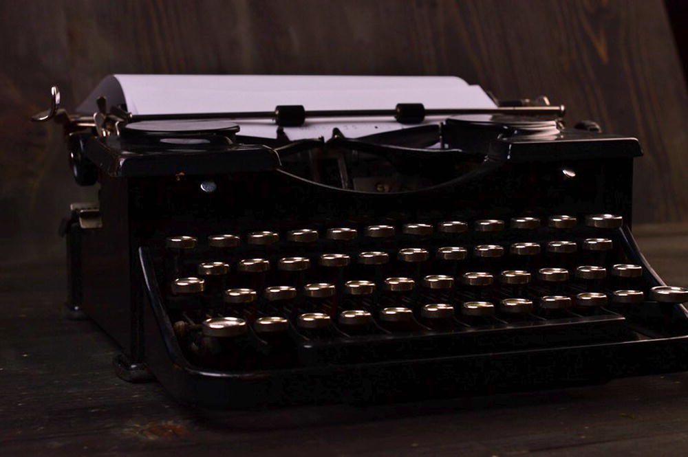 A photograph of an ancient typewriting machine. It has a paper roll on it.