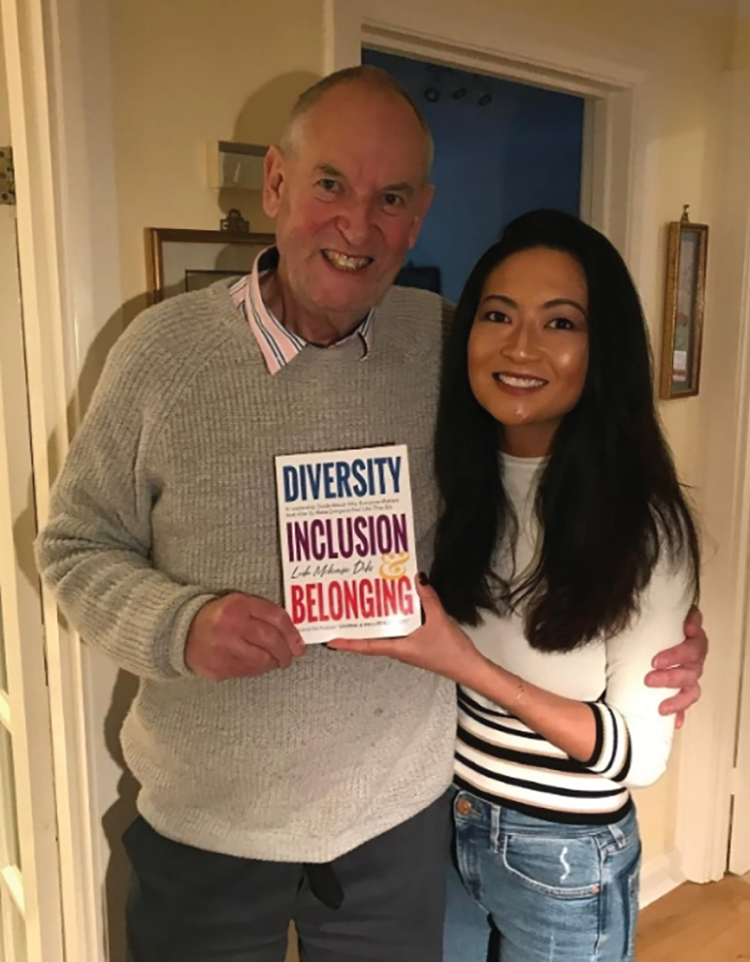 A photograph of a man embracing a woman with one hand, both of them displaying a book titled 'Diversity, Inclusion, and Belonging'.