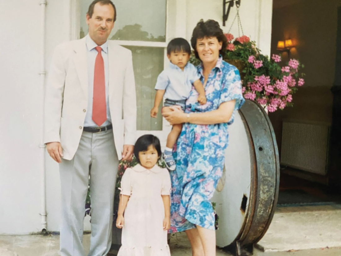 A photograph captures a scene featuring a man, a woman, a young woman, and a young man. A woman is carrying the young man in her hands.