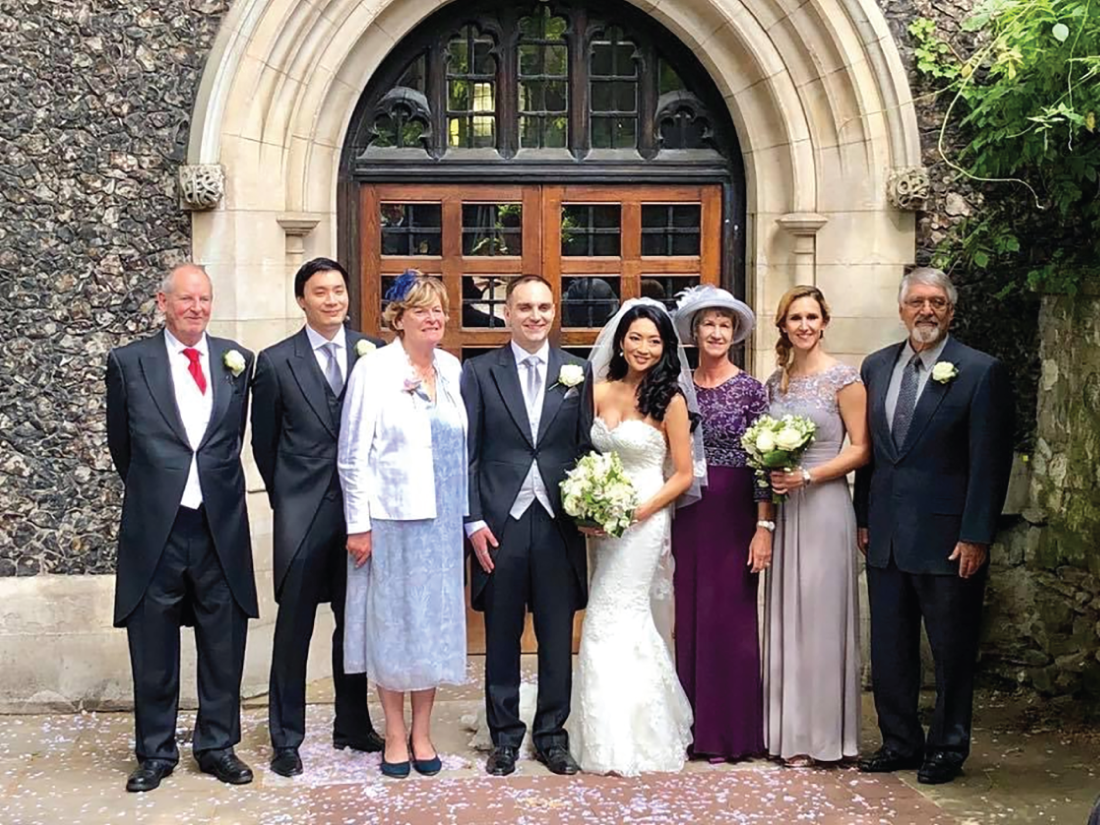 A photograph depicts four men and four women. Two of the women are holding flower bouquets in their hands.