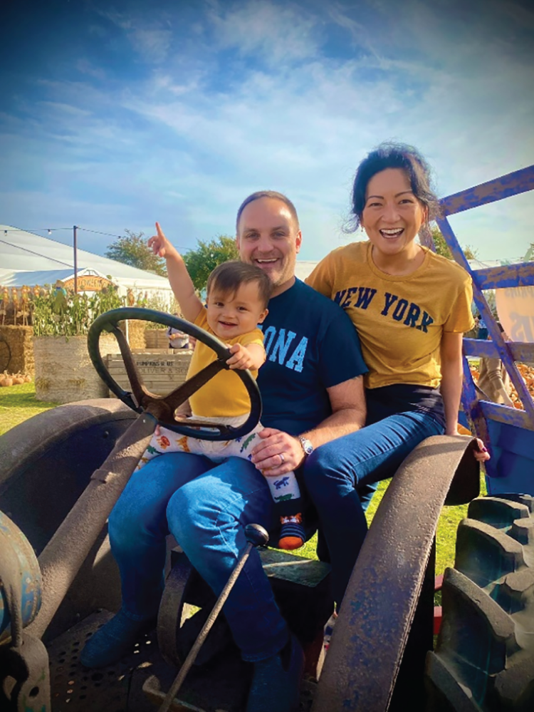 A photograph captures a scene with a man, a woman, and a young man sitting together in a tractor. The young man is seated on the man.