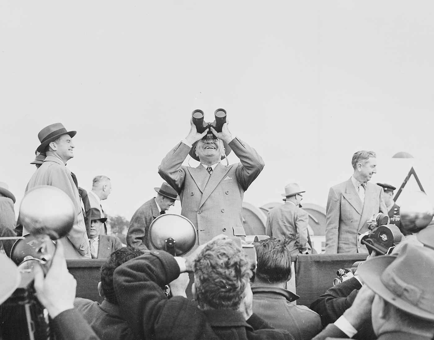 Photograph of President Truman using binoculars to observe an aerial display during an air show at Andrews Air Force